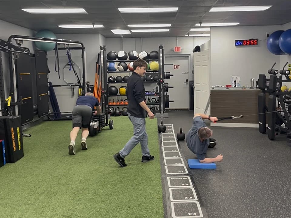 A coach cueing a member through a side plank while another member pushes the sled at 838 Strength and Fitness in Monroe, CT
